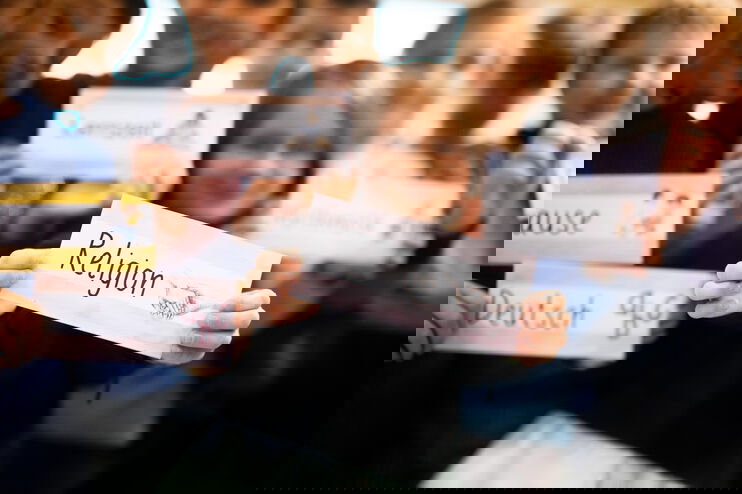 Kinder halten Schilder mit Schulfächern in die Kamera, im Mittelpunkt: Religion