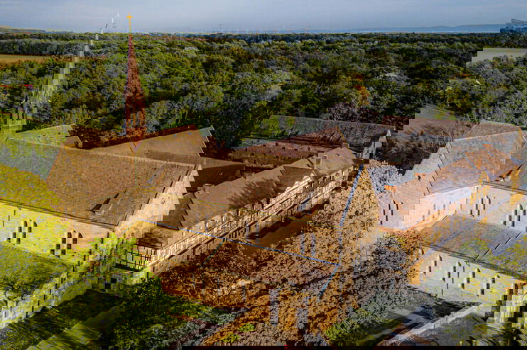 Eine große historische Kirche mit angrenzenden Fachwerkgebäuden inmitten mehrerer Bäume.