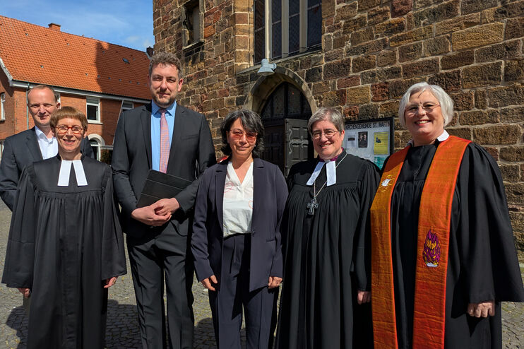 Eine Gruppe aus als Frauen und Männer lesbaren Personen, teils im Talar, vor einem Backsteingebäude.
