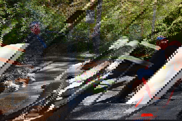 Eine als Frau lesbare Person mit kurzen Haaren steht im Freien an einem Redepult und spricht vor Publikum.