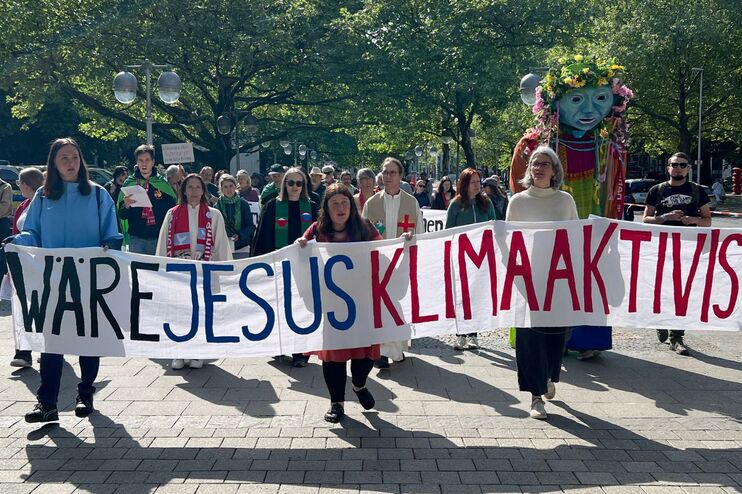 Menschen auf einer Demonstration, sie halten ein Banner, auf dem steht "Wäre Jesus Klimaaktivist?".