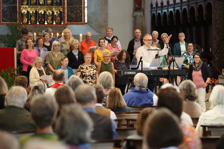 Ein Chor und eine Kirchengemeinde singen gemeinsam, ein Chorleiter dirigiert.