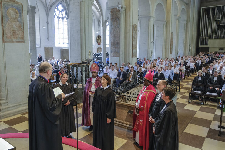 Mehrere Menschen im geistlichen Gewand stehen im Altarraum einer vollbesetzten Kirche.