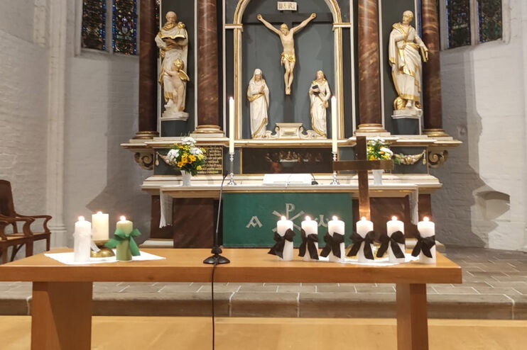 Ein Tisch mit mehreren Kerzen mit Trauerflor vor einem Altar