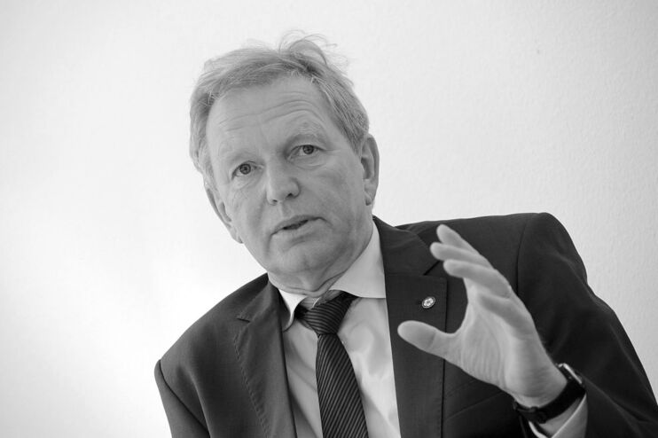 Schwarz-weiß-Bild einer als Mann lesbaren Person, die mit erhobener Hand spricht.