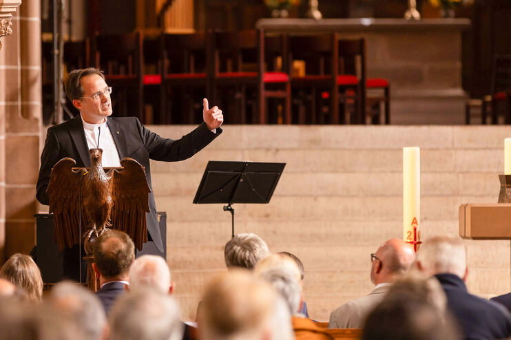 Eine als Mann lesbare Person im Anzug spricht vor Publikum in einer Kirche