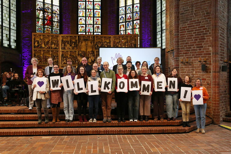 Eine große Gruppe hält in einer Kirche Buchstaben hoch, die das Wort Willkommen ergeben