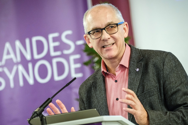 Eine männlich lesbare Person steht an einem Rednerpult und spricht.