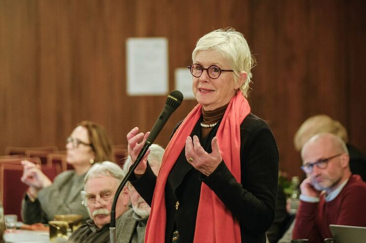 Eine als Frau lesbare Person mit rotem Schal spricht in ein Mikrofon.