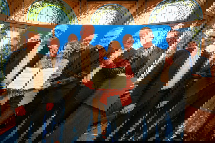 Ein Gruppe von weiblich und männlich zu lesenden Personen steht in einem Halbkreis und in der Mitte halten drei Personen ein Schriftstück in die Höhe.