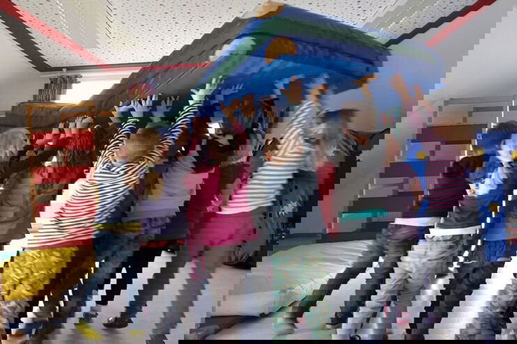 Mehrere Kinder stemmen gemeinsam eine Matratze in die Höhe.