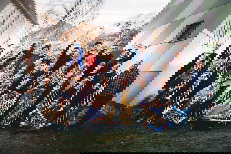 Etwa dreißig junge Menschen stehen und knien zusammen für ein Gruppenfoto, sie halten Blasinstrumente in Händen.