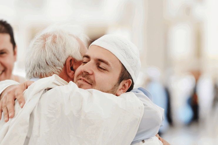 Zwei in weiß gekleidete Männer umarmen sich und lächeln dabei.