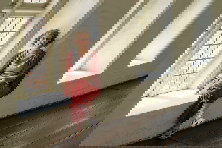 Eine Frau sitzt in einem Fenster im Kreuzgang eines Klosters.