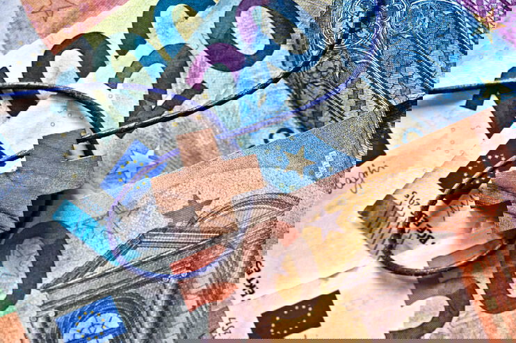 Auf Euro-Banknoten liegt ein Holzkreuz an einer Kette.