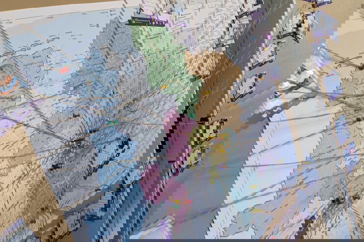 An einer braunen Pinnwand hängt eine bunte Karten von Niedersachsen. Bindfäden verbinden einige Orte mit lila Karten, auf denen Namen und Fotos sind. 