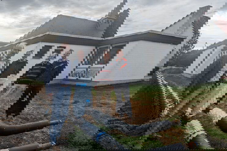 Vier Menschen stehen vor einem Gebäude und schauen sich sich große schwarze Rohre an.