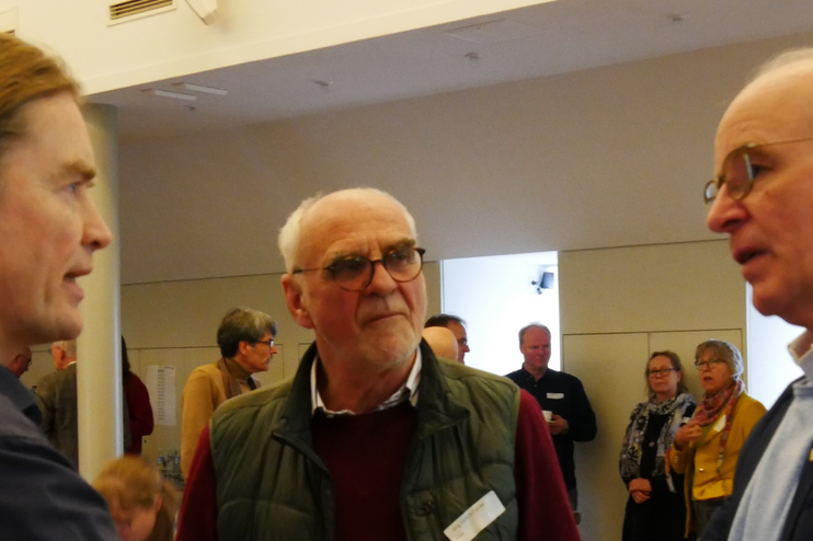 Drei Personen stehen zusammen im Gespräch. Die mittlere hält eine Kaffeetasse in Händen.