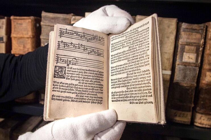 Zwei Hände mit weißen Handschuhen halten ein sehr altes Gesangbuch.