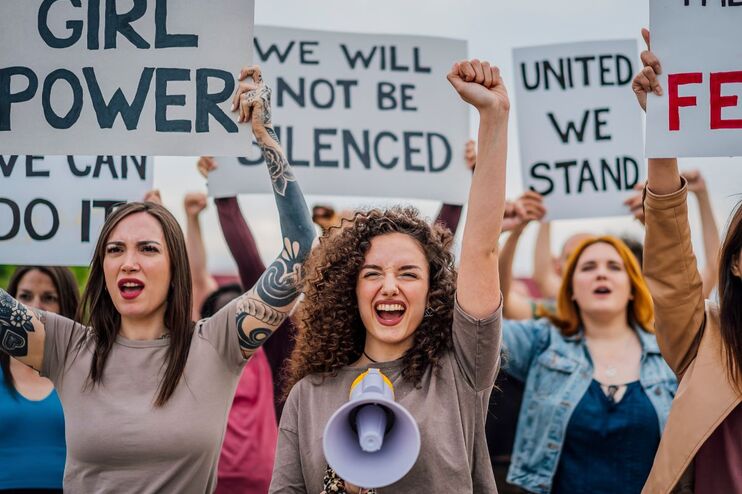 Junge, weiblich gelesene Personen demonstrieren mit Plakaten, auf denen steht: Girl power - Frauenpower, We will not be silenced - Wir werden nicht leise gestellt, United we stand - Wir stehen gemeinsam