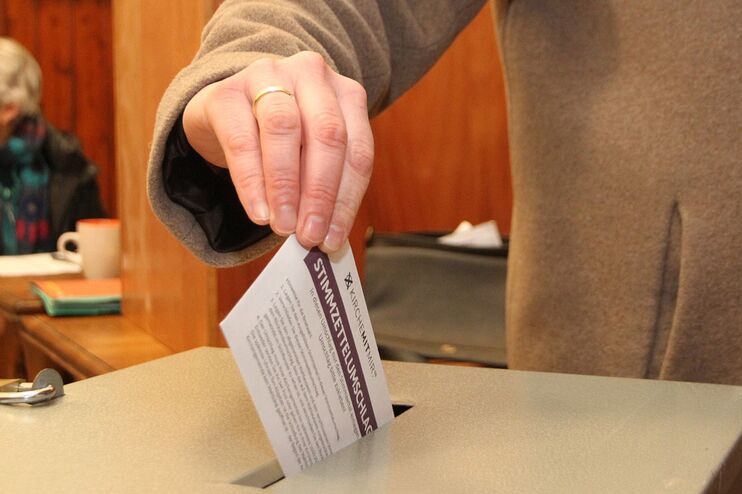 Eine Hand wirft einen Zettel in eine Urne. 