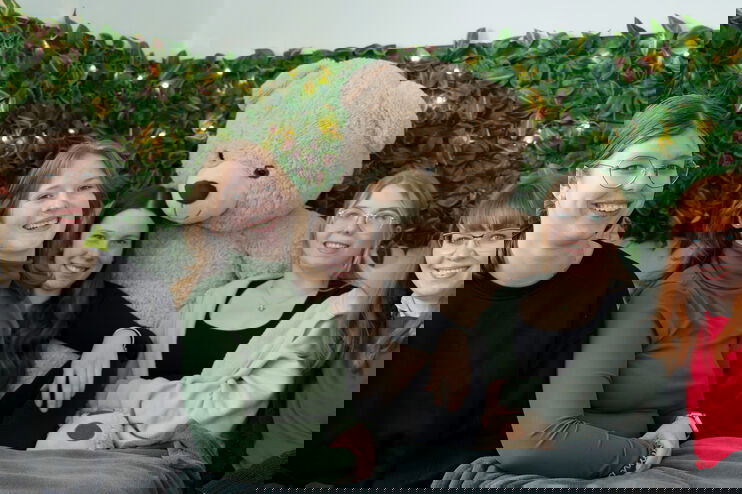 Fünf als Mädchen lesbare Personen sitzen mit einem Teddy in der Sofa-Ecke eines Jugendtreffs.