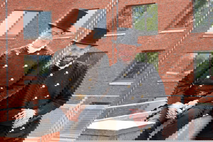 Eine als Frau lesbare Schornsteinfegerin und ein als Mann lesbarer Schornsteinfeger stehen auf einem Dach.