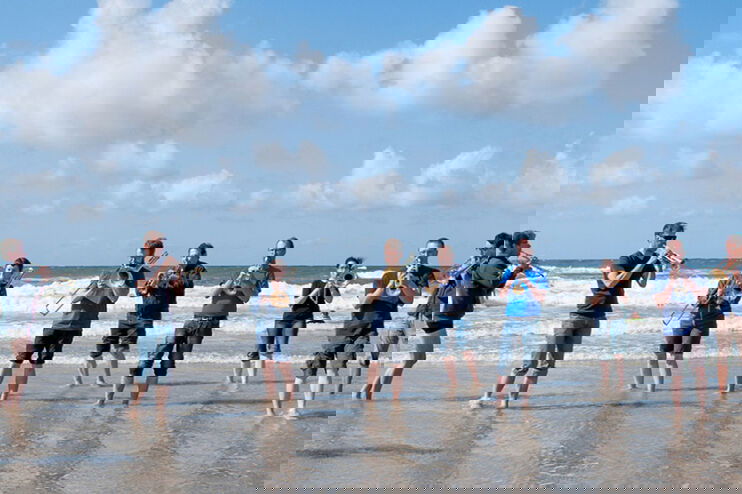 eine Blaesercombo steht mit den Fuessen im Meer und spielt bei Sonnenschein Musik