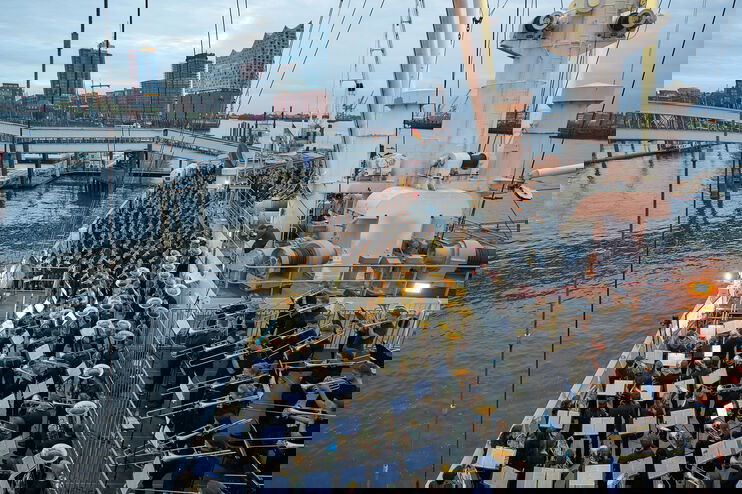 Ein riesige Blasensemble spielt auf einem Schiff, im Hintergrund ist die Hamburger Elbphilharmonie zu sehen.