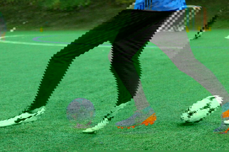 Auf einem Fußballplatz spielt jemand den Ball.