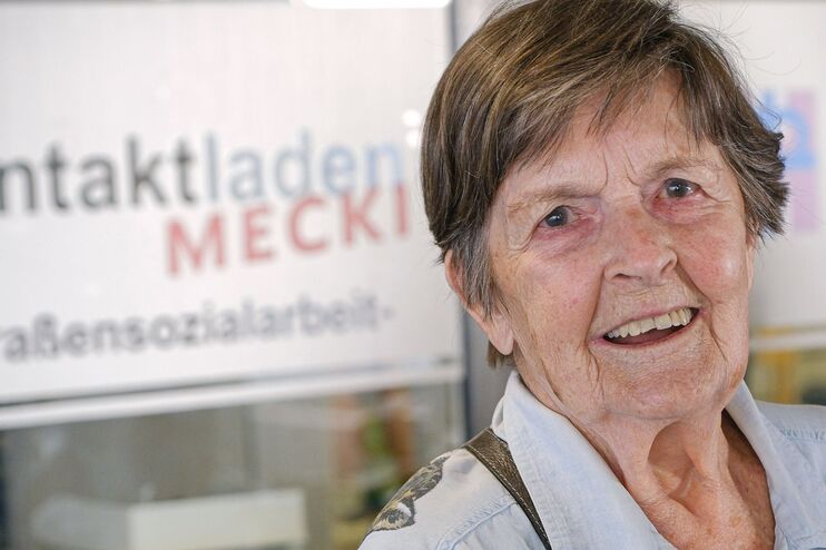 Eine ältere Dame mit kurzen grauen Haaren und einer blauen Bluse steht vor dem Kontaktladen Mecki. Dort hilft die 96-Jährige ehrenamtlich Wohnungslosen.