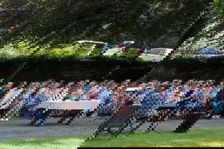 Viele Menschen sitzen im Freien, rechts steht eine Person im Talar, weiter links ein Altar.