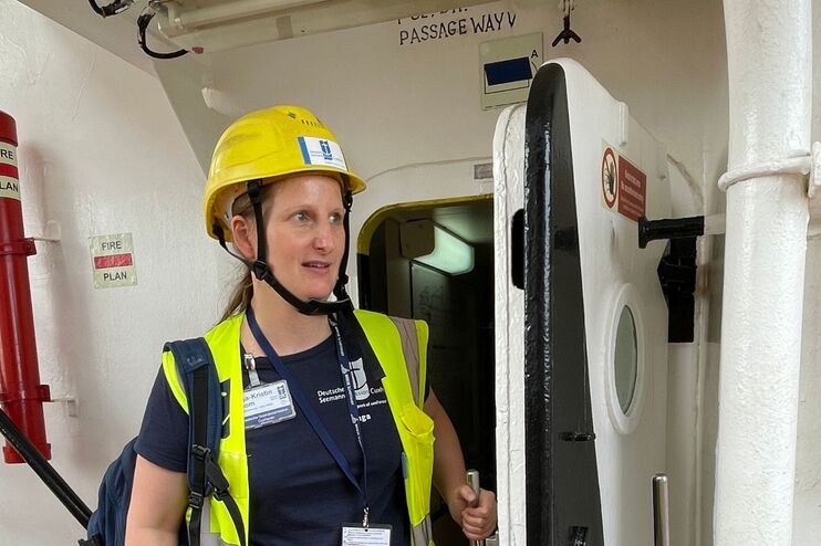 Eine weiblich gelesene Person steht mit Helm und Warnweste auf einem Schiffsdeck.