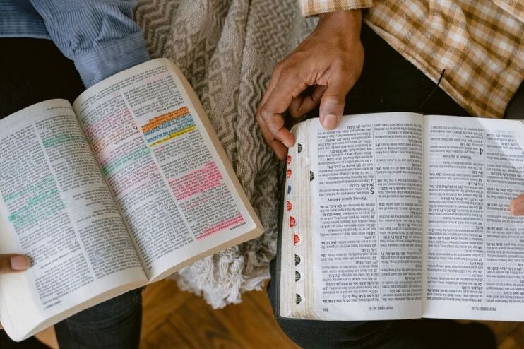 Zwei Menschen sitzen nebeneinander, man sieht aufgeschlagene Bibeln auf ihren Schößen, bei denen einzelnen Passagen farbig markiert sind. 