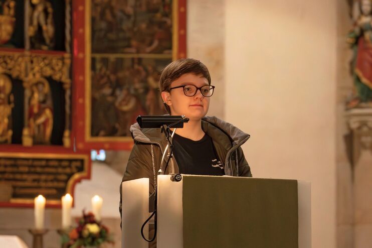 Ein Mädchen mit kurzen Haaren und einer Brille steht vor einem Altar an einem Rednerpult.