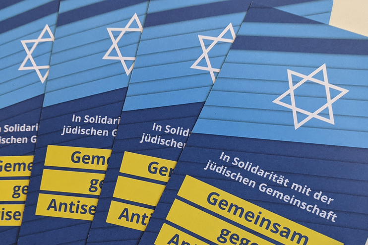 Mehrere Flyer liegen in Reihe. Er zeigt einen weißen Davidstern auf blauem Untergrund. Darunter steht: In Solidarität mit der jüdischen Gemeinschaft - Gemeinsam gegen Antisemitismus