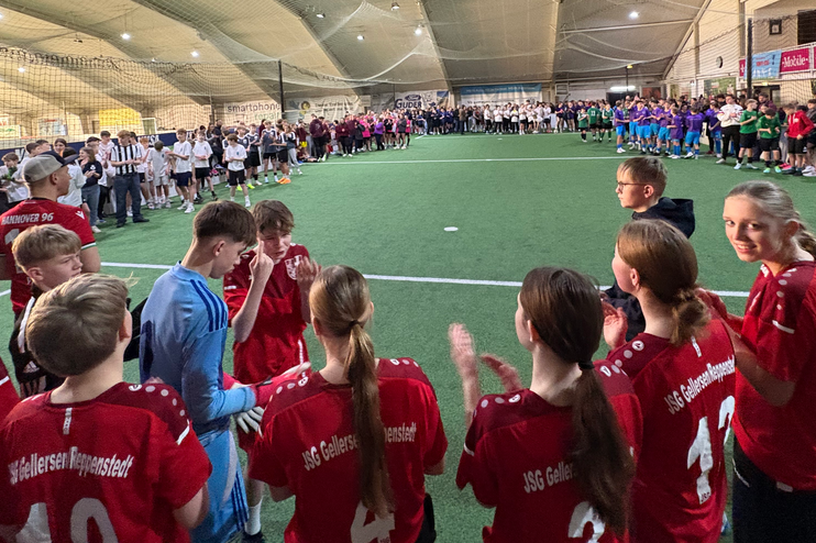 Blick in eine Halle mit Fußballfeldern, junge Menschen in unterschiedlichen Trikots stehen um ein Feld herum.