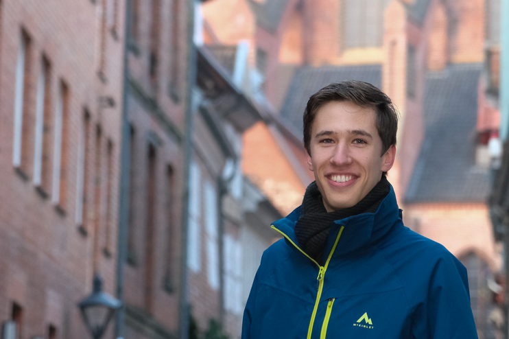 Eine junge, männlich gelesene Person in blauer Jacke lächelt fröhlich.