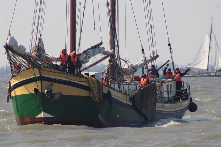 Ein Segelschiff auf Wasser mit mehreren Masten und Menschen an Bord.
