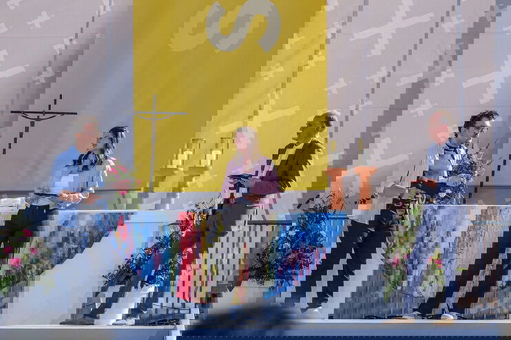 Zwei als Männer und eine als Frau lesbare Personen im Gespräch auf einer großen Bühne.