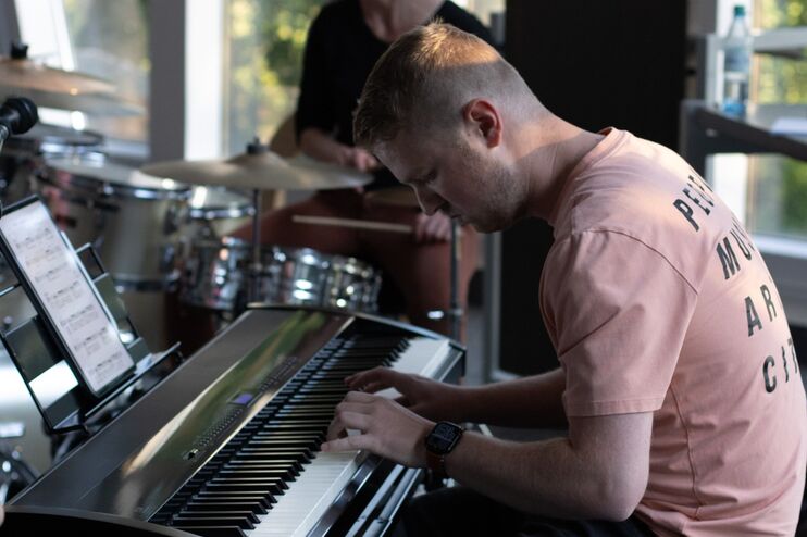 Eine männlich gelesene Person in orange-rosa Shirt sitzt an einem Keyboard.