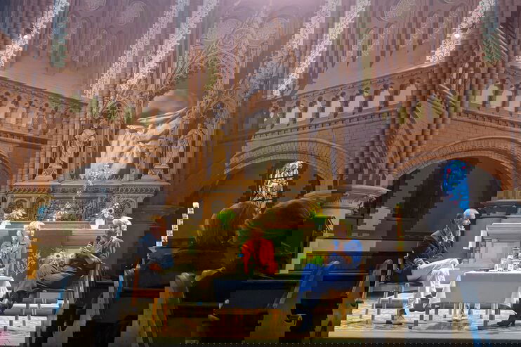 Zwei weiblich und eine männlich gelesene Person sitzen im Altarraum einer Kirche vor Publikum. 