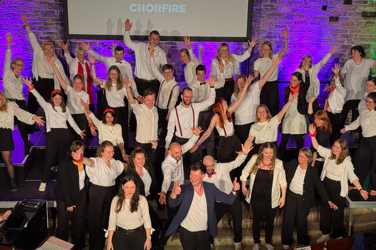 Etwa zwei Dutzend Menschen in dunklen Hosen und weißen Hemden stehen zusammen und heben die Hände.