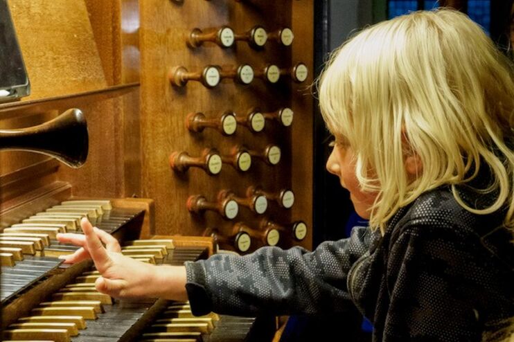 Ein blondes Kind spielt mit einer Hand auf einer Orgel-Tastatur.