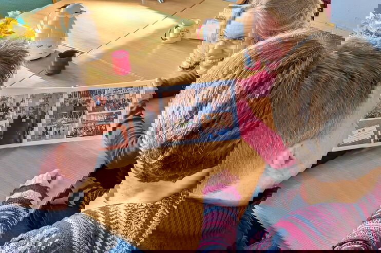 Drei Personen sitzen an einem Tisch und schauen in ein Fotobuch.