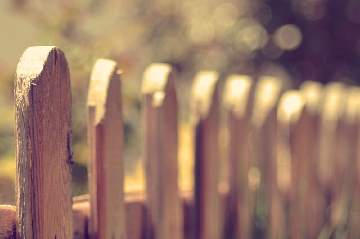 Ein Zaun aus Holz, zwischen den Latten sieht man etwas Garten.
