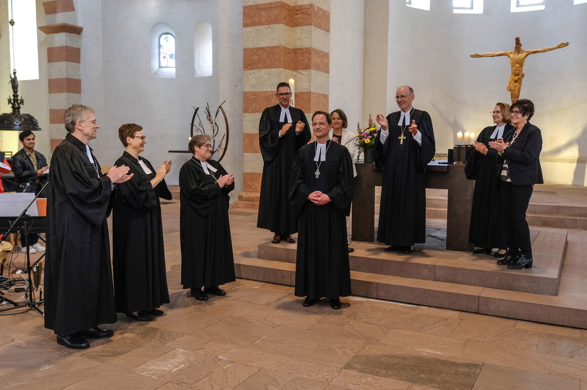 Mehrere als Männer und Frauen lesbare Personen stehen in einem Altarraum und applaudieren.