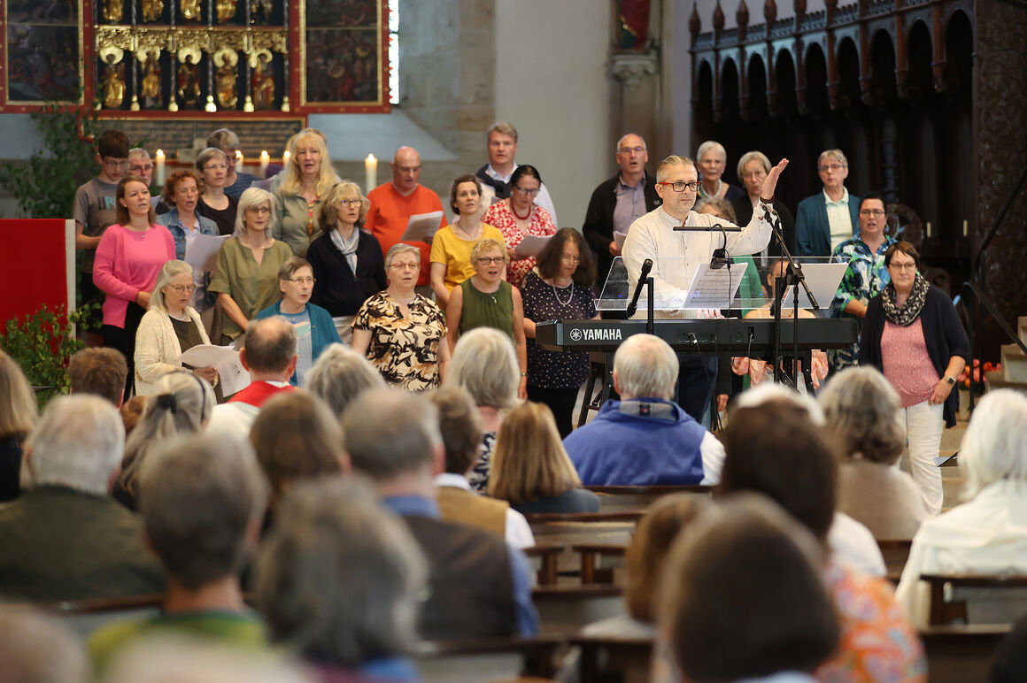 Ein Chor und eine Kirchengemeinde singen gemeinsam, ein Chorleiter dirigiert.