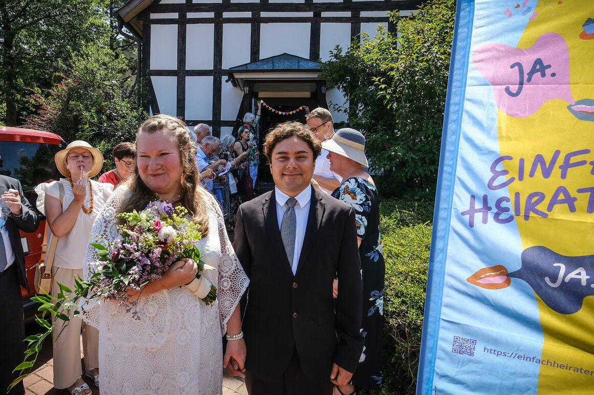 Eine Hochzeitsgesellschaft begrüßt ein Paar, das aus der Kirche kommt.