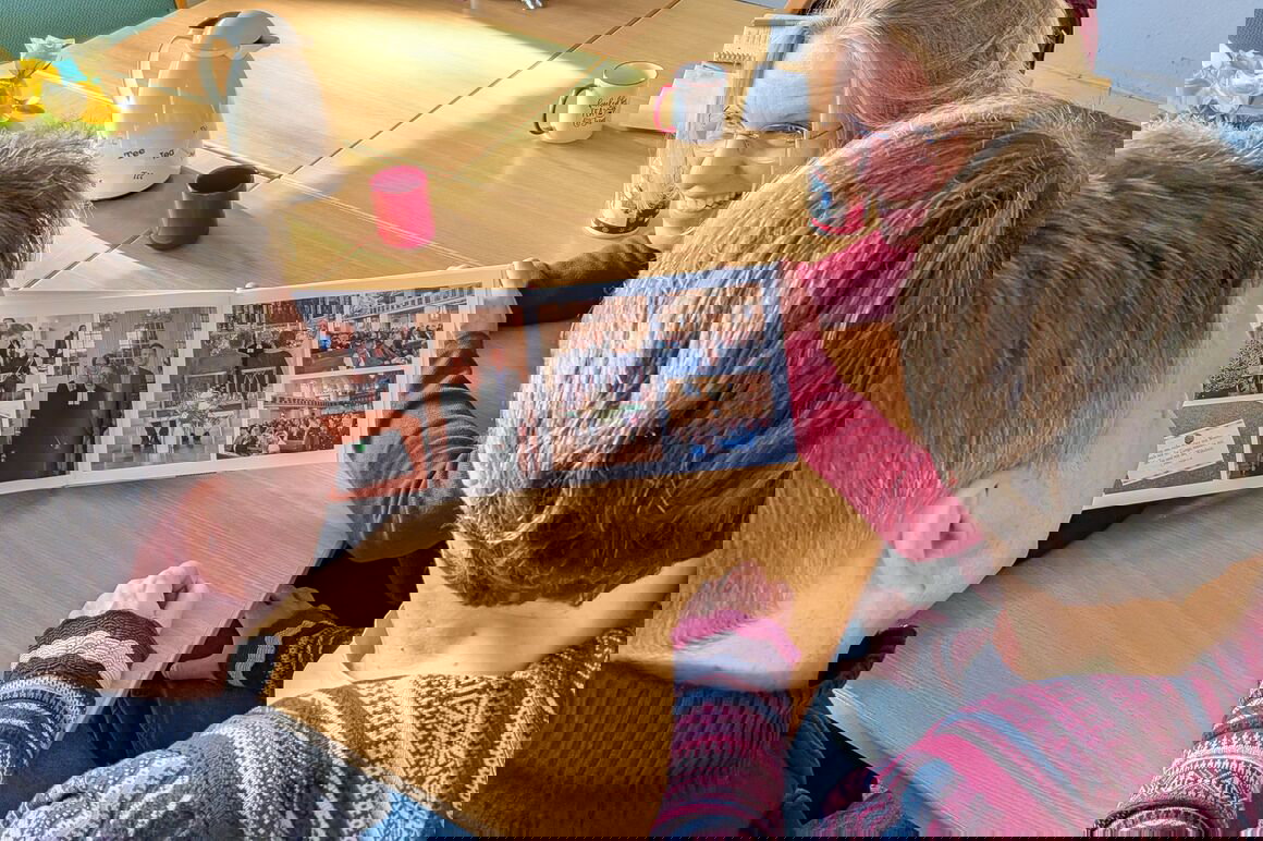 Drei Personen sitzen an einem Tisch und schauen in ein Fotobuch.